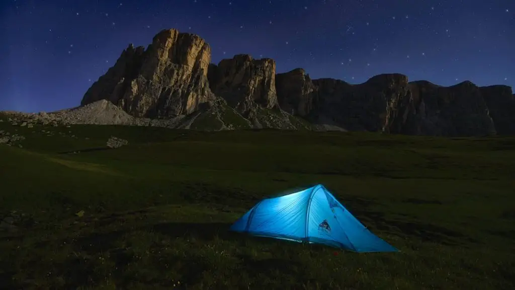 What is a Backpacking Tent Footprint with tent on the grass by a awesome rock formation at night.