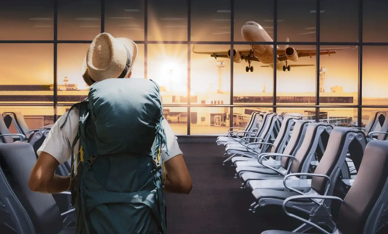 Travel tourist standing with backpack watching sunset at airport window. Passenger seat in departure lounge for see airplane, View from airport terminal.