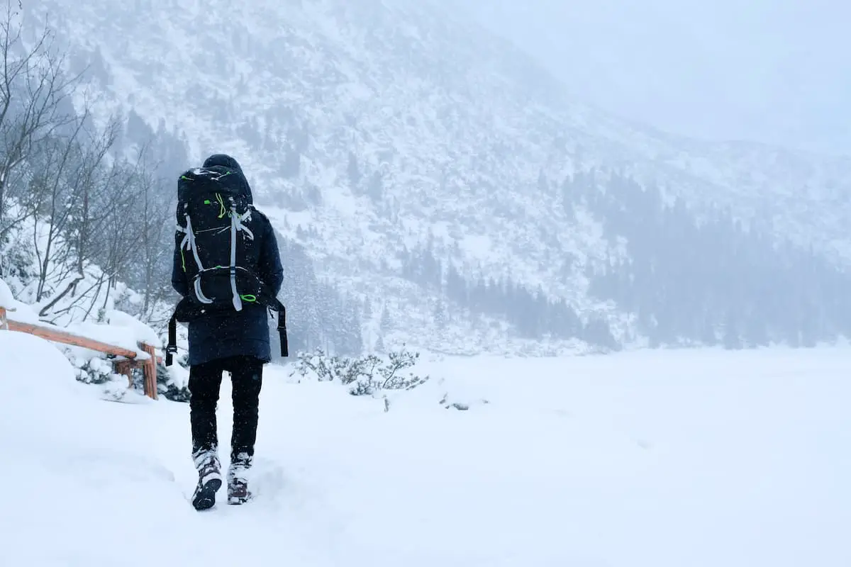 A man hiking on a cold snowy hill, with boots and gloves and full thru hiking backpack setup