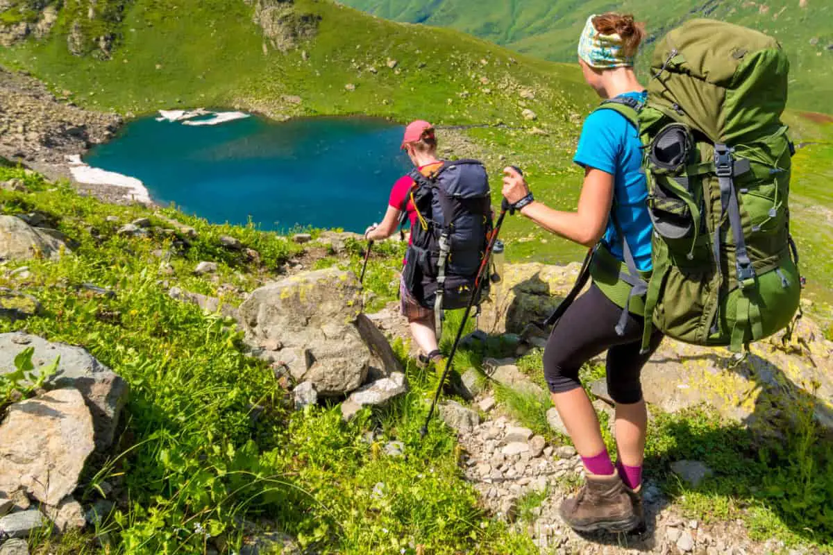 Photo is of two ladies with large 60L backpacks who are hiking down to a lake.