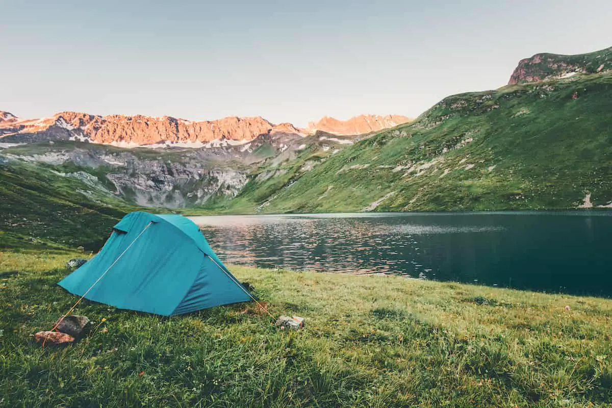 blue tent on the grass located by a lake and surrounded by amazing mountains.